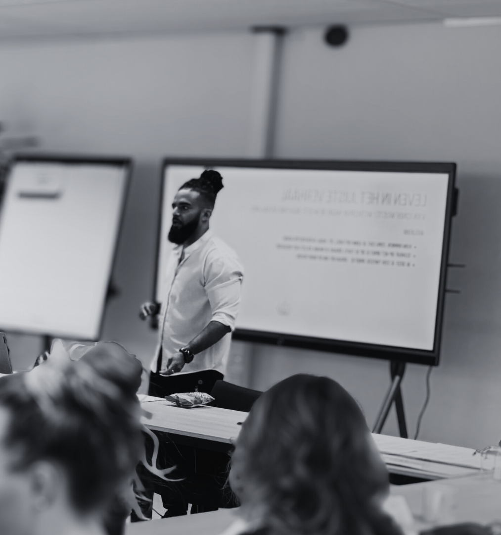 Person giving a presentation in a classroom setting with screens and audience.