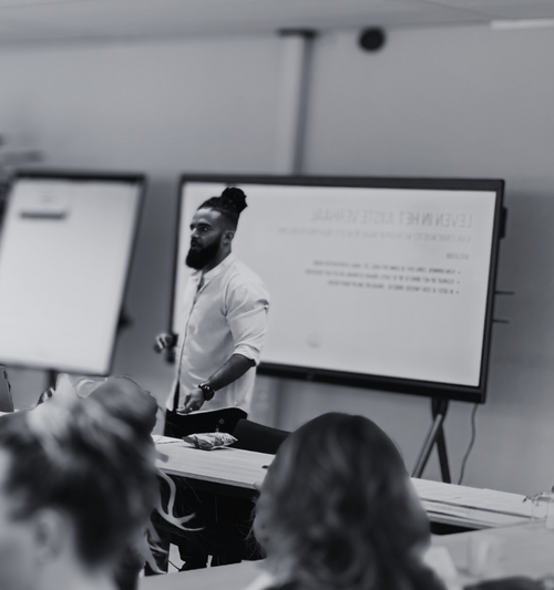 Person giving a presentation in a classroom setting with screens and audience.